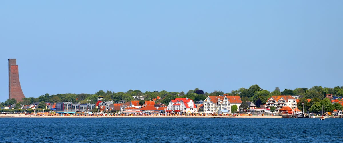 A coastal town with a prominent tower, red-roofed buildings, and a beach.