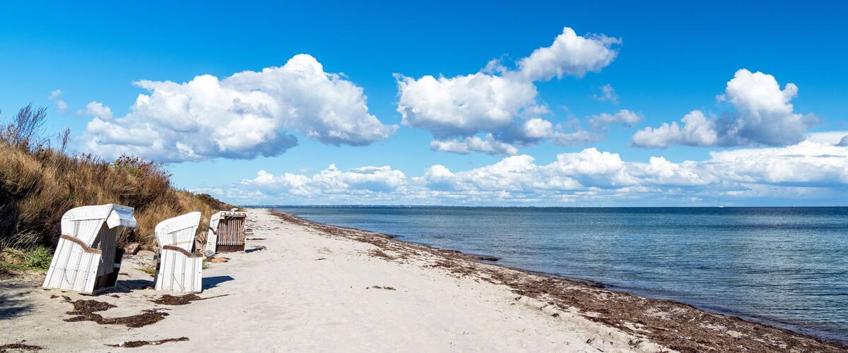 A beach with white wicker chairs and a clear blue sky.