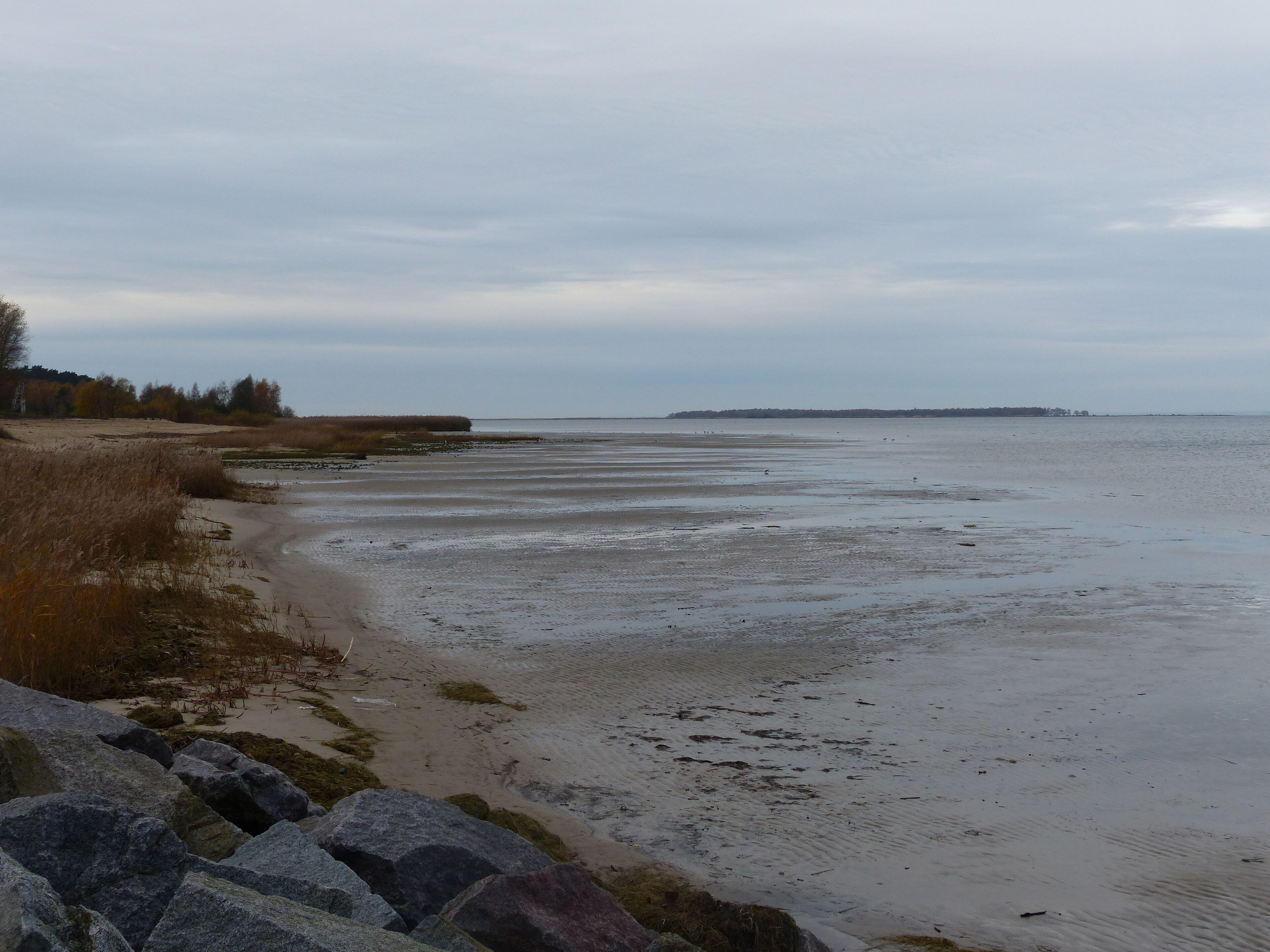 A coastal landscape with a sandy beach, rocky outcrops, and a distant shoreline.