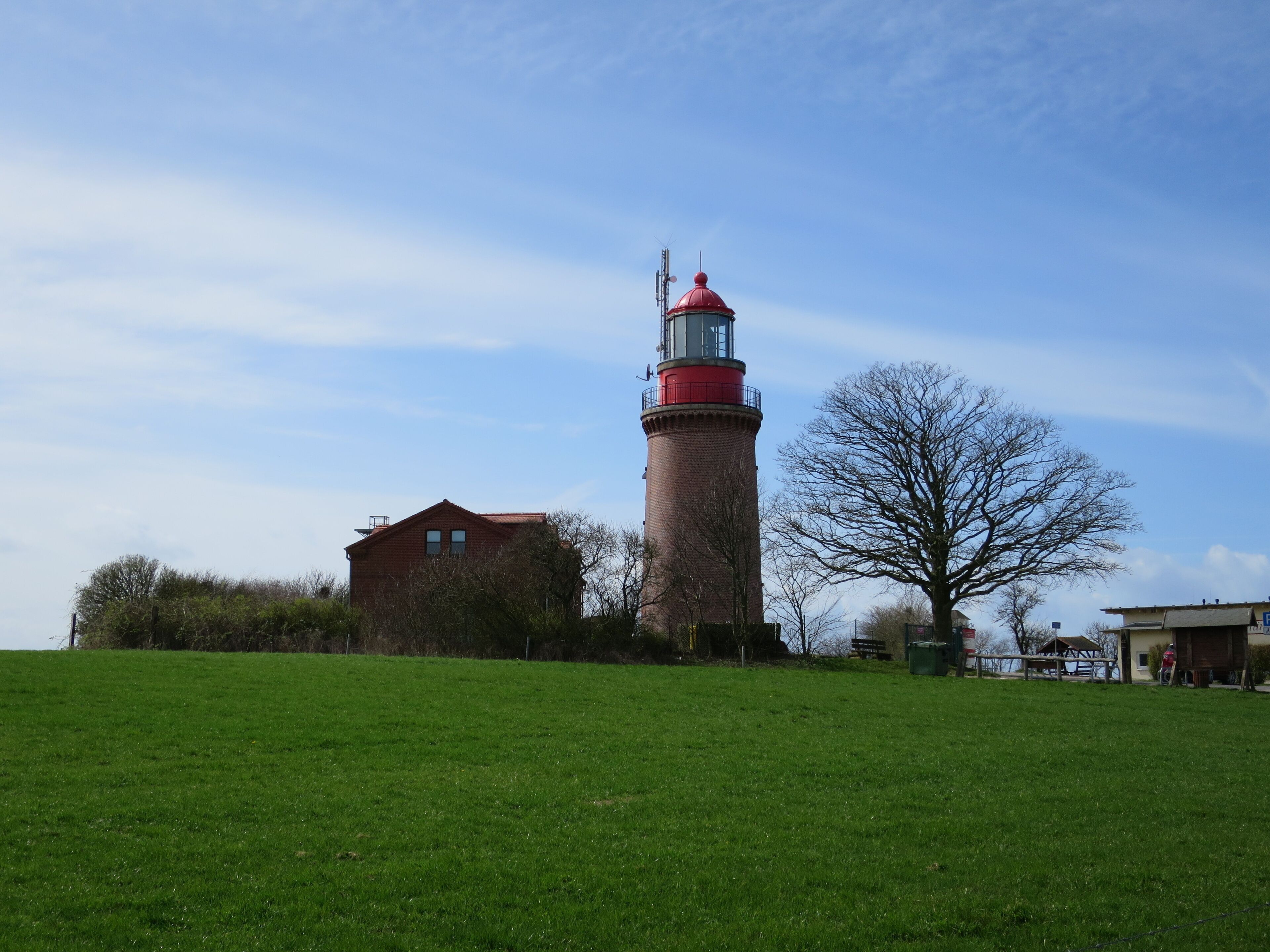 A lighthouse, a brick building, and a tree in a grassy field.