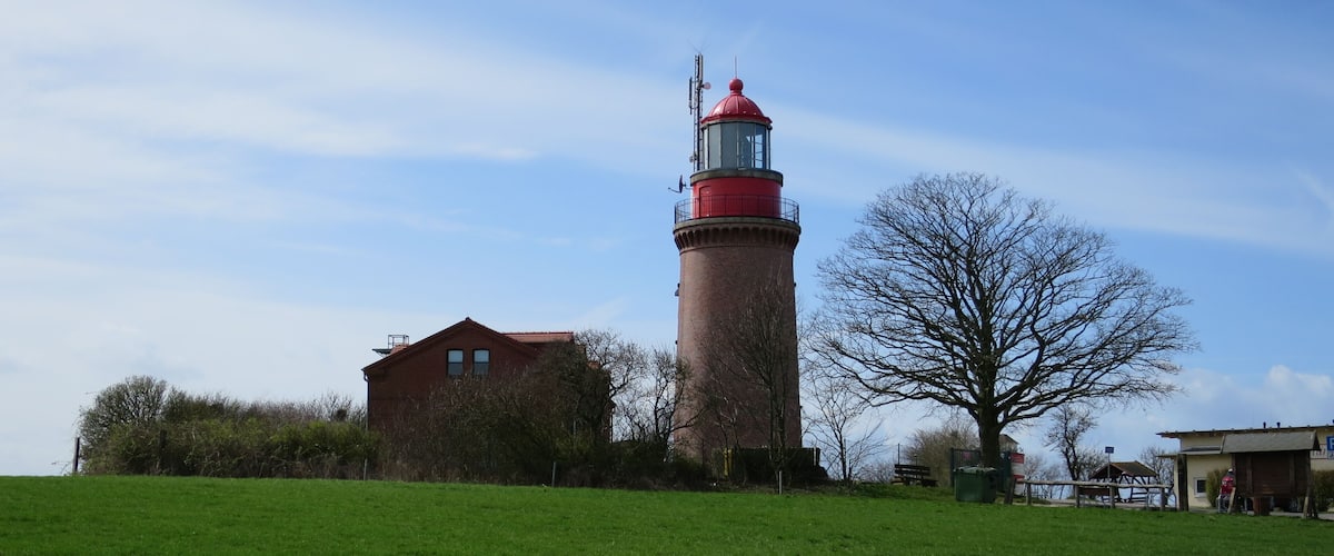 A lighthouse, a brick building, and a tree in a grassy field.