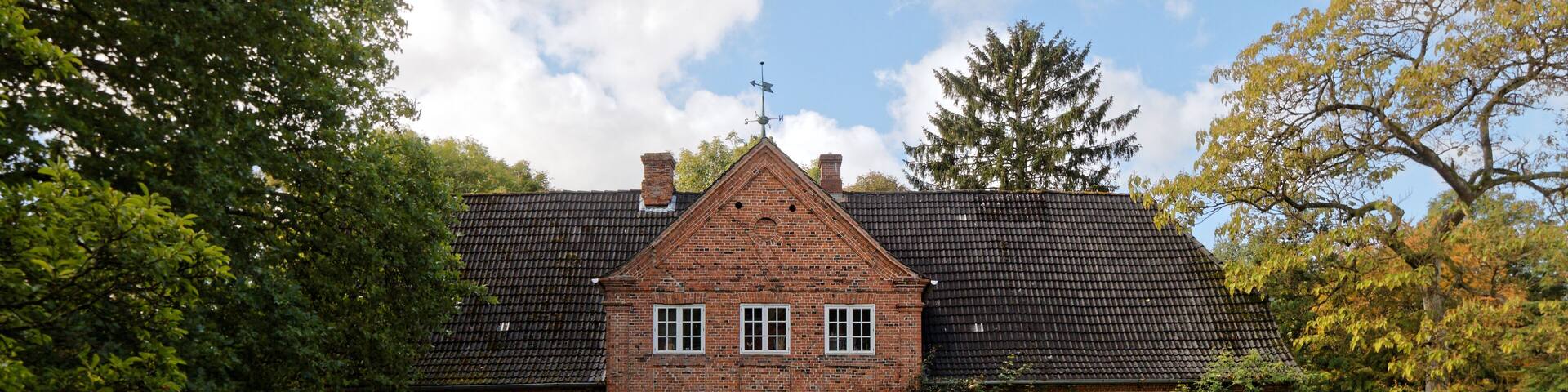 A large brick house with a tiled roof, surrounded by a well-maintained lawn and trees.