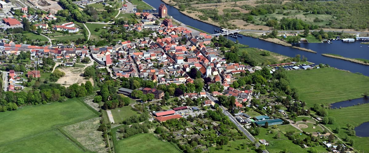 An aerial view of a town with a river, green fields, and a church.