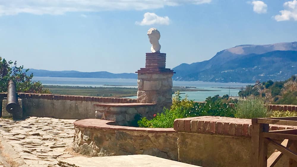 Un fort côtier doté d’une statue, de murs en pierre et offrant une vue sur la mer et les montagnes.