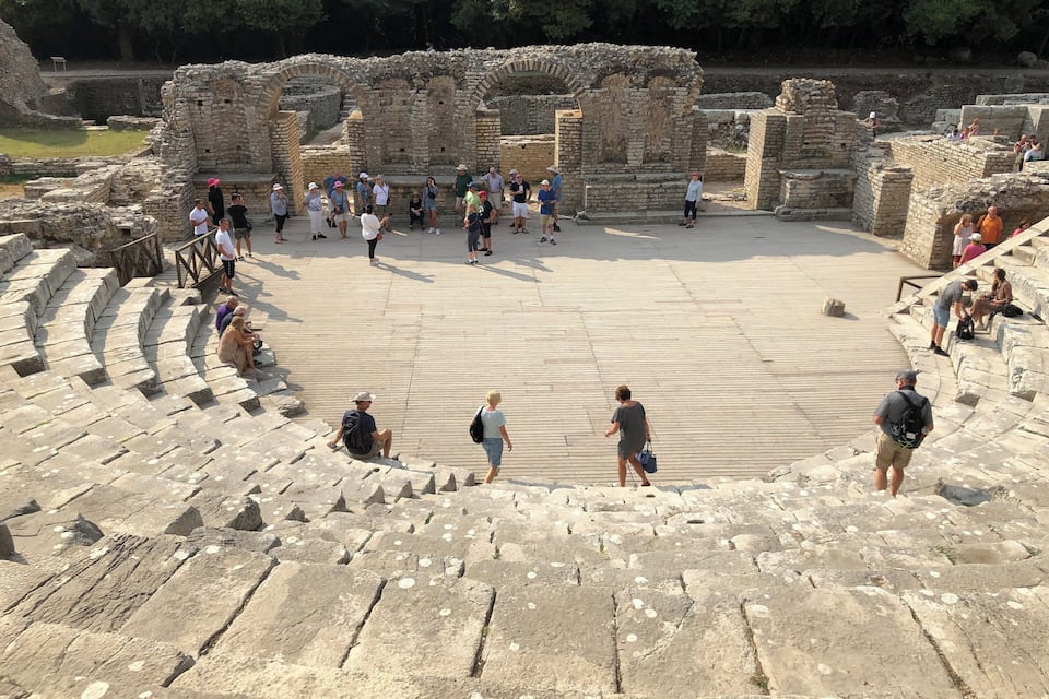 Un antiguo anfiteatro con asientos de piedra y ruinas al fondo.