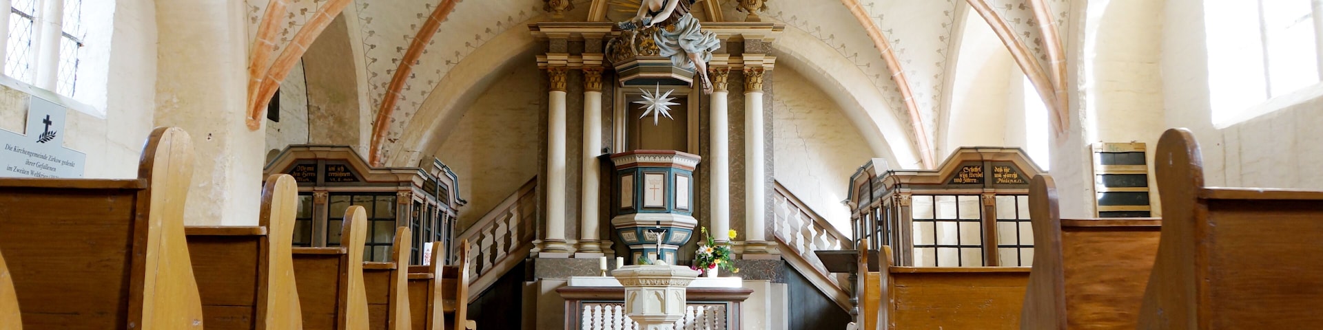 Un interior con techos abovedados, bancos de madera y un altar central con una estatua.