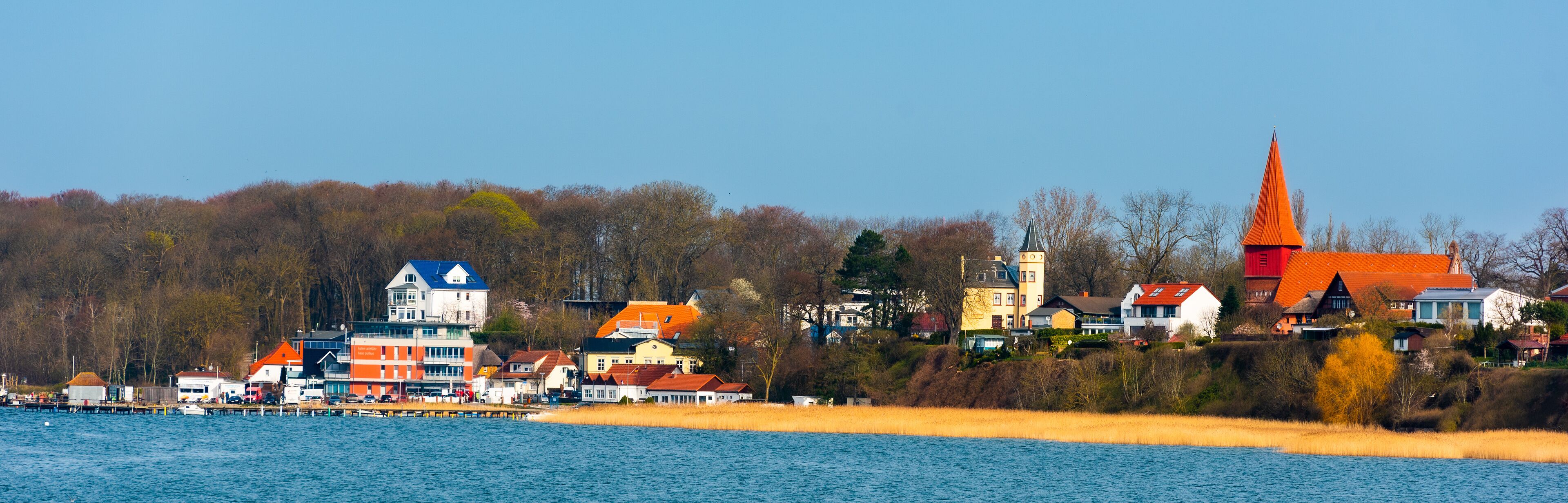 A lakeside town with colorful houses, a church with a tall spire, and a pier with boats.