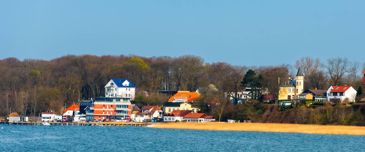 A lakeside town with colorful houses, a church with a tall spire, and a pier with boats.