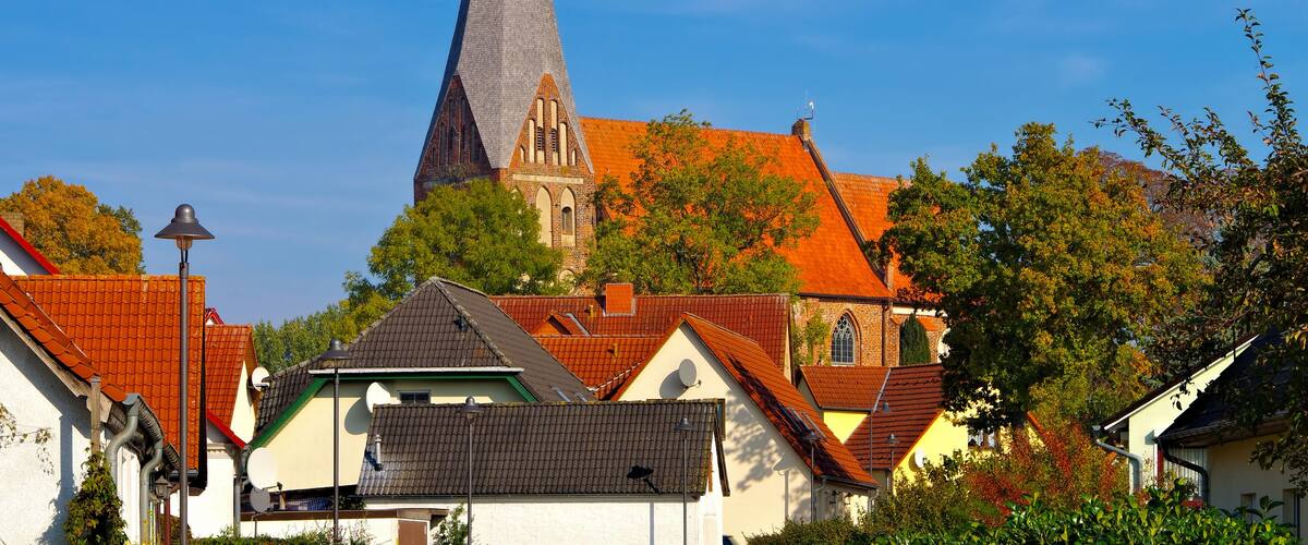 A church with a tall spire and red-tiled roofs, surrounded by residential buildings and trees.