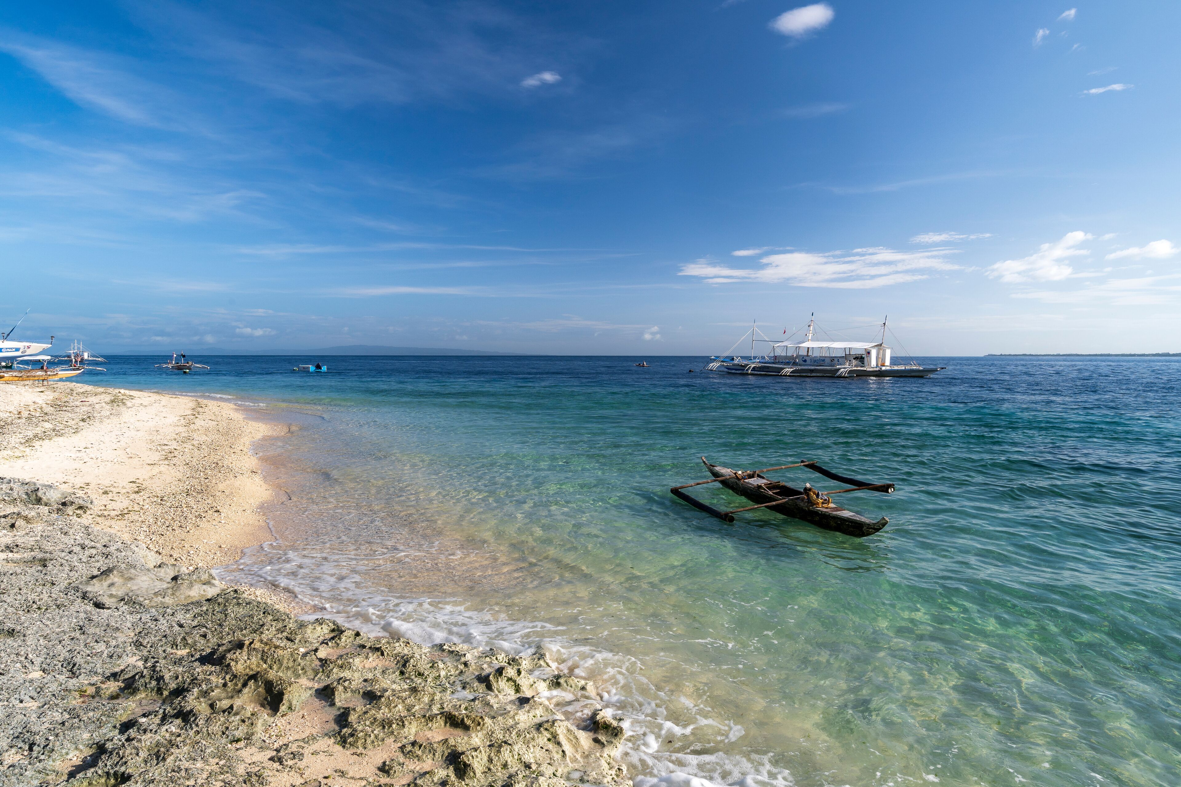 A beach with clear water, boats, and a rocky shoreline.