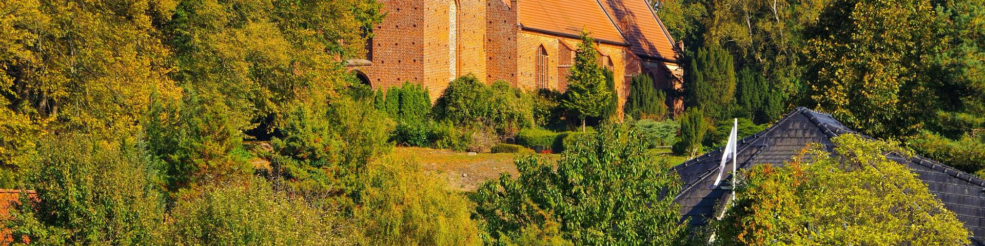 A church with a red roof and a tower, surrounded by autumn-colored trees.
