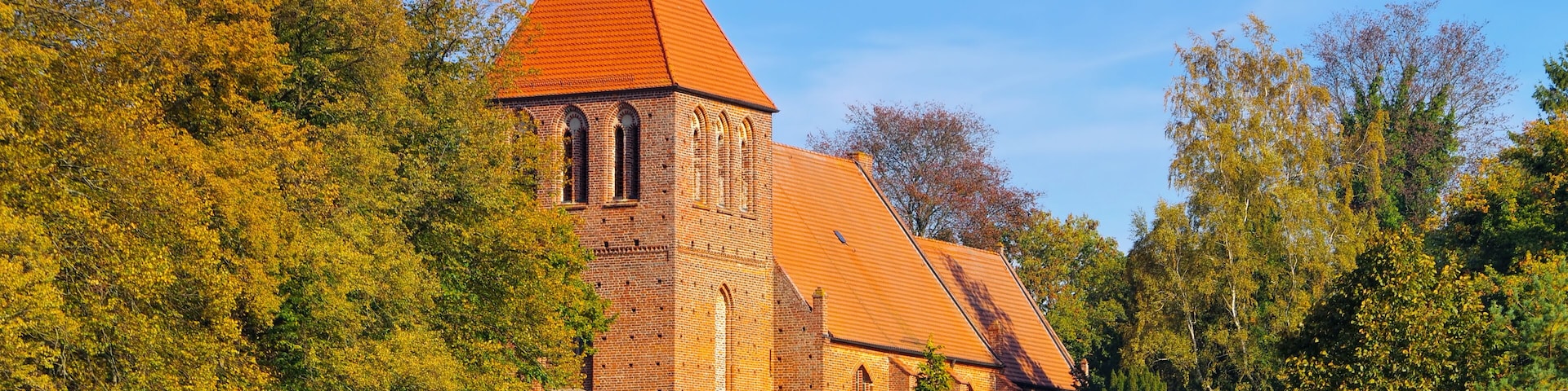A church with a red roof and a tower, surrounded by autumn-colored trees.