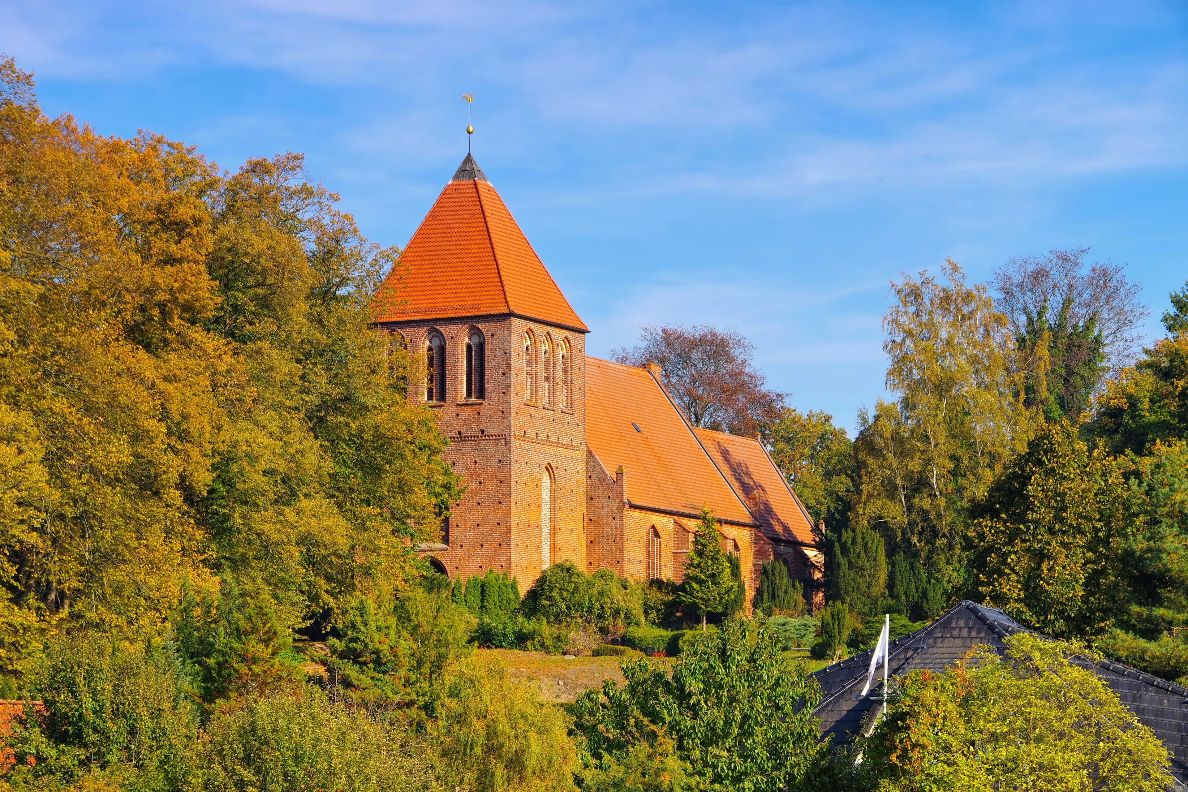 A church with a red roof and a tower, surrounded by autumn-colored trees.