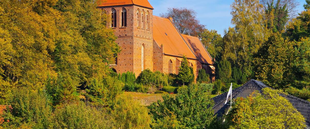 A church with a red roof and a tower, surrounded by autumn-colored trees.