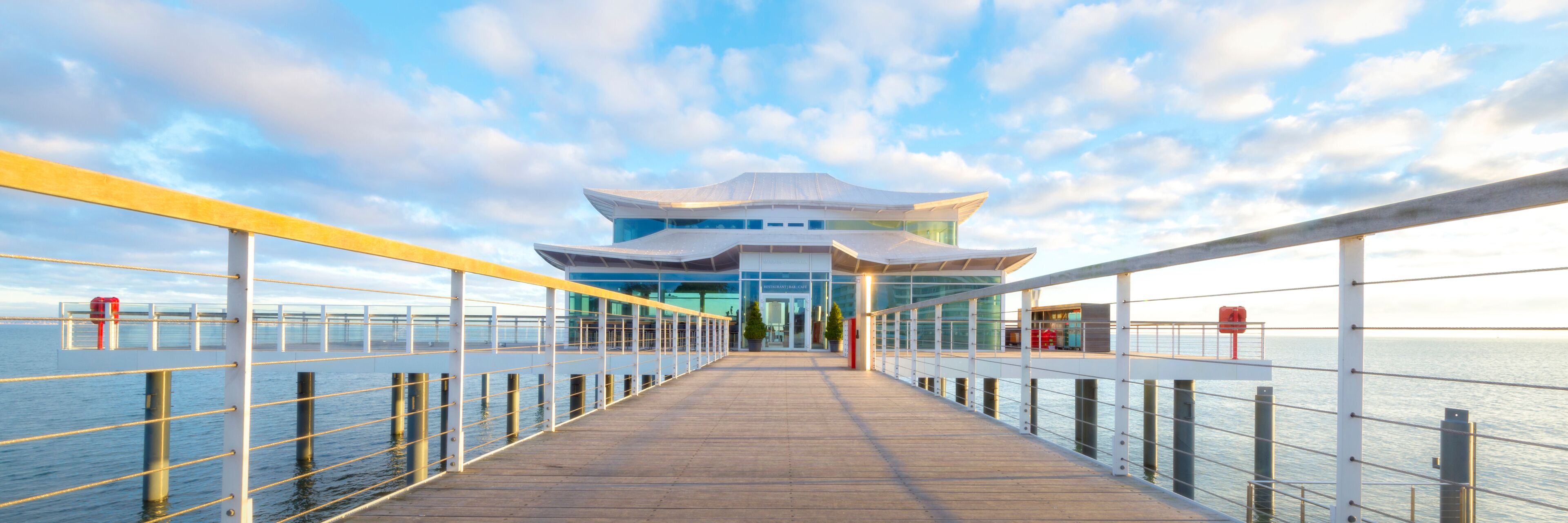 A waterfront promenade leading to a modern building with a distinctive architectural design.