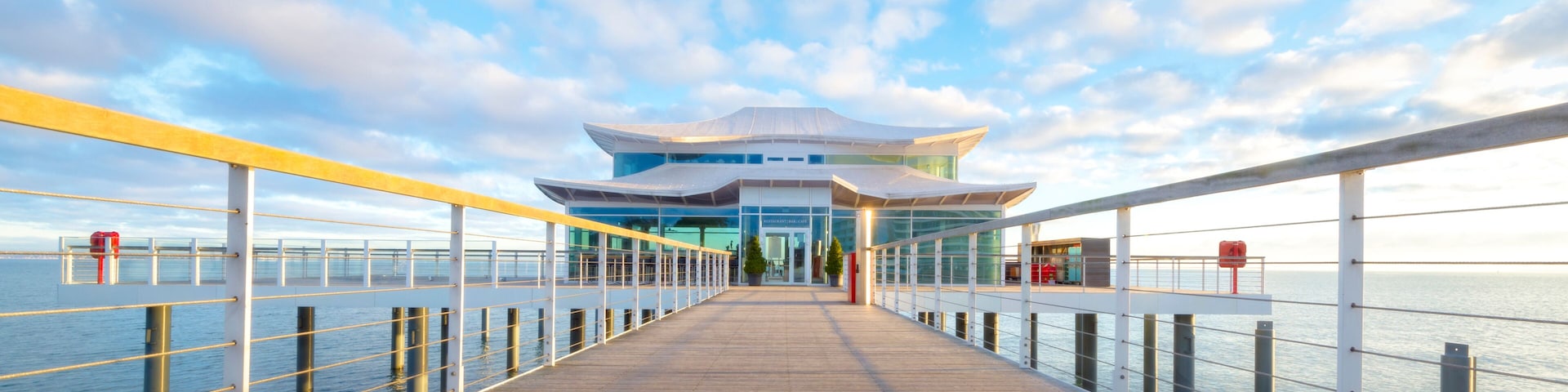 A waterfront promenade leading to a modern building with a distinctive architectural design.