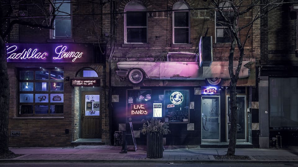 Um carro antigo sobre um edifício, letreiros de neon e fachada de tijolos.