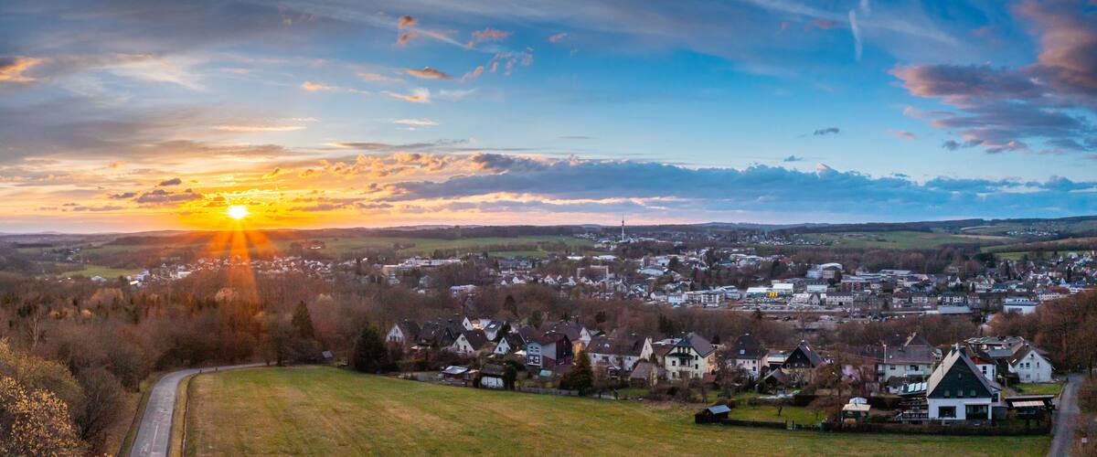 A sunset over a town with a prominent church steeple, surrounded by houses and a forested area.