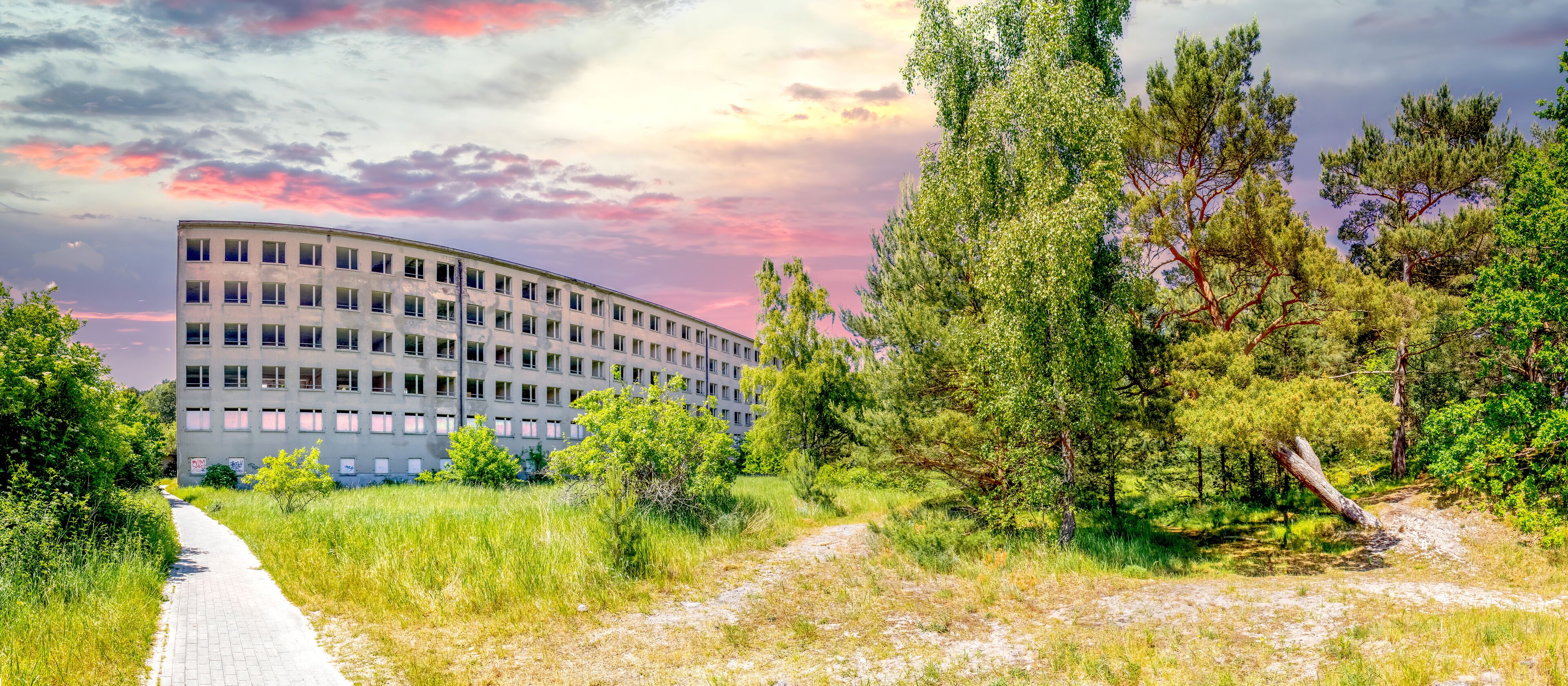 A curved building surrounded by trees and a gravel path.