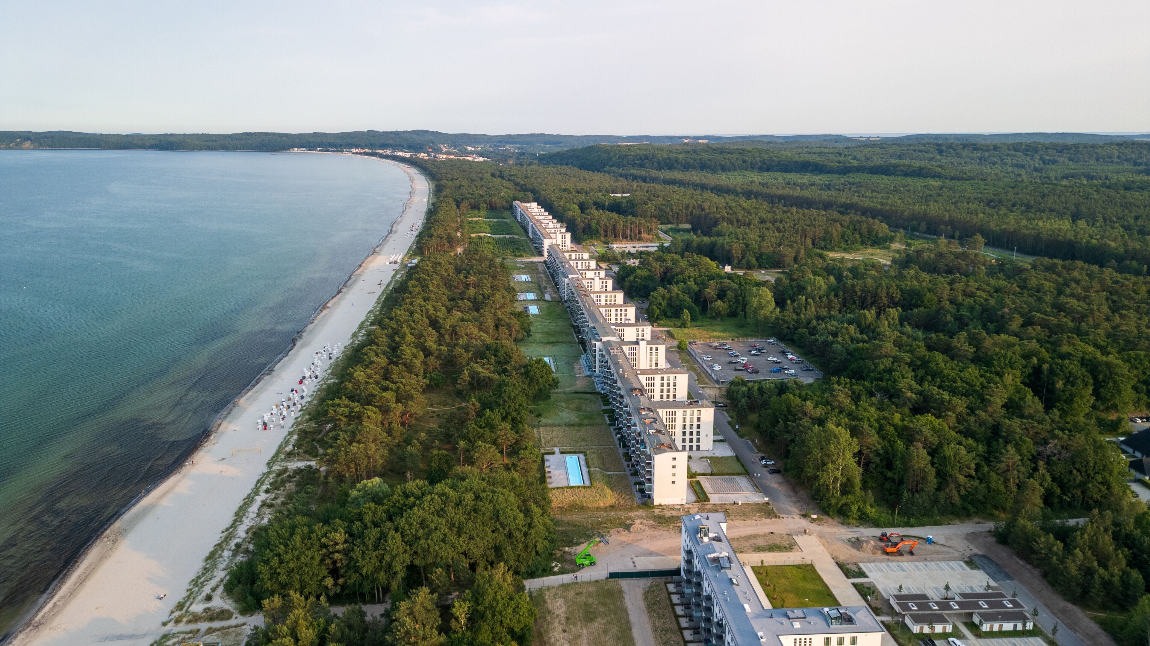A coastal resort with a long beachfront, dense forest, and a row of modern buildings.