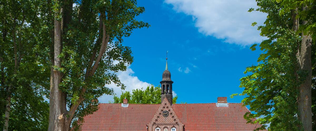 A brick building with a tower, surrounded by trees and a clear blue sky.