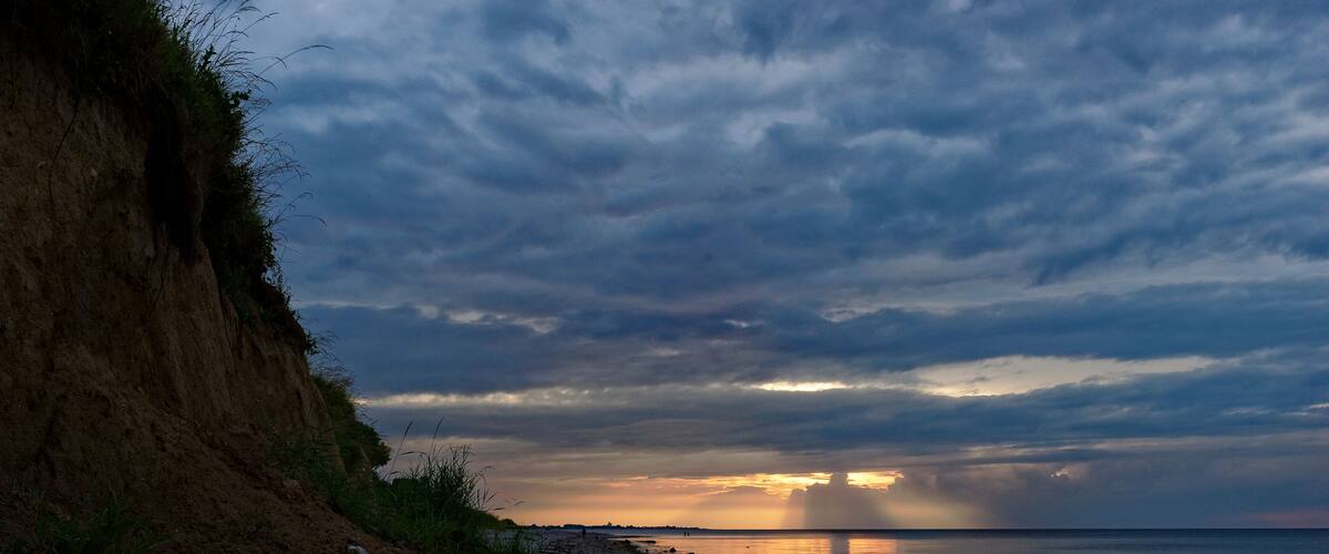 A rocky shoreline with a cliff on the left and a sunset over the water.