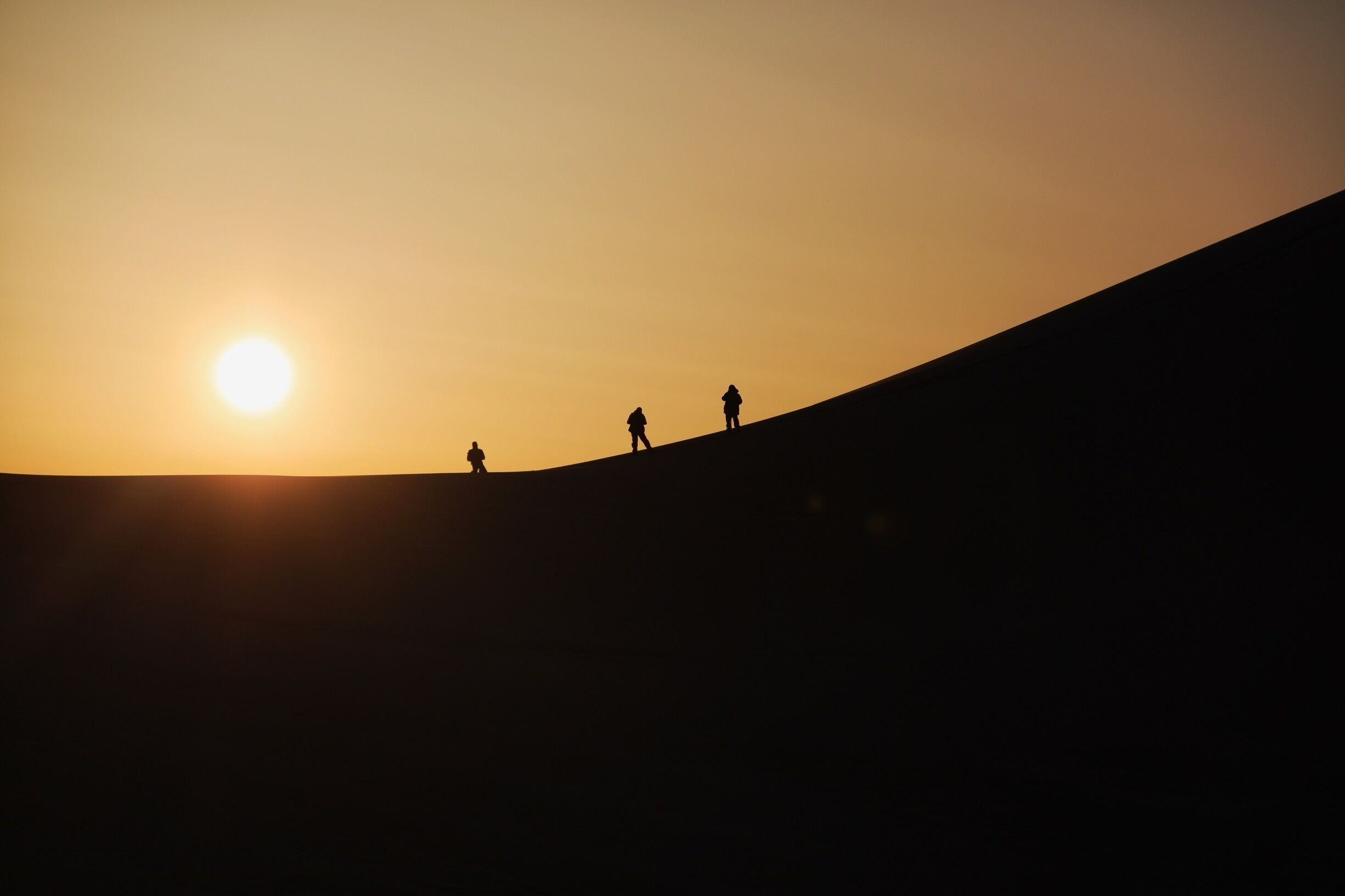 A sunset over a hill with three silhouetted figures.