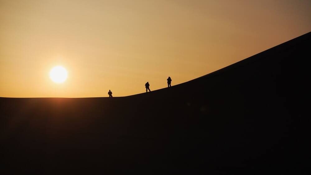A sunset over a hill with three silhouetted figures.