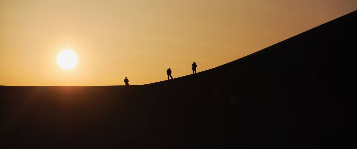 Un atardecer sobre una colina con tres figuras silueteadas.
