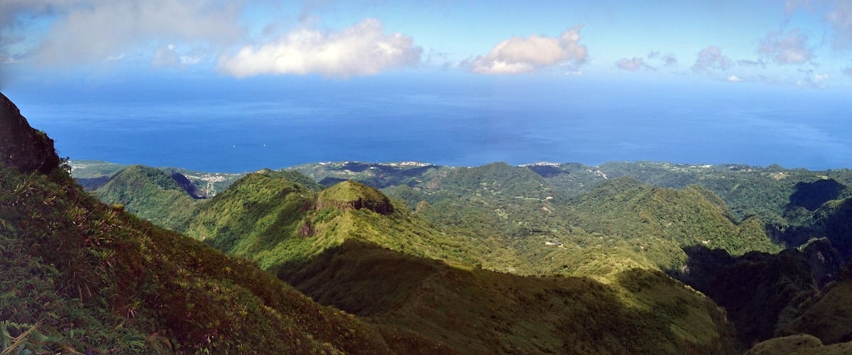 A mountainous landscape with lush greenery and a view of the ocean.