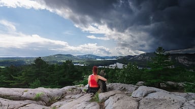 A person sitting on rocks overlooking a lake surrounded by mountains and trees.