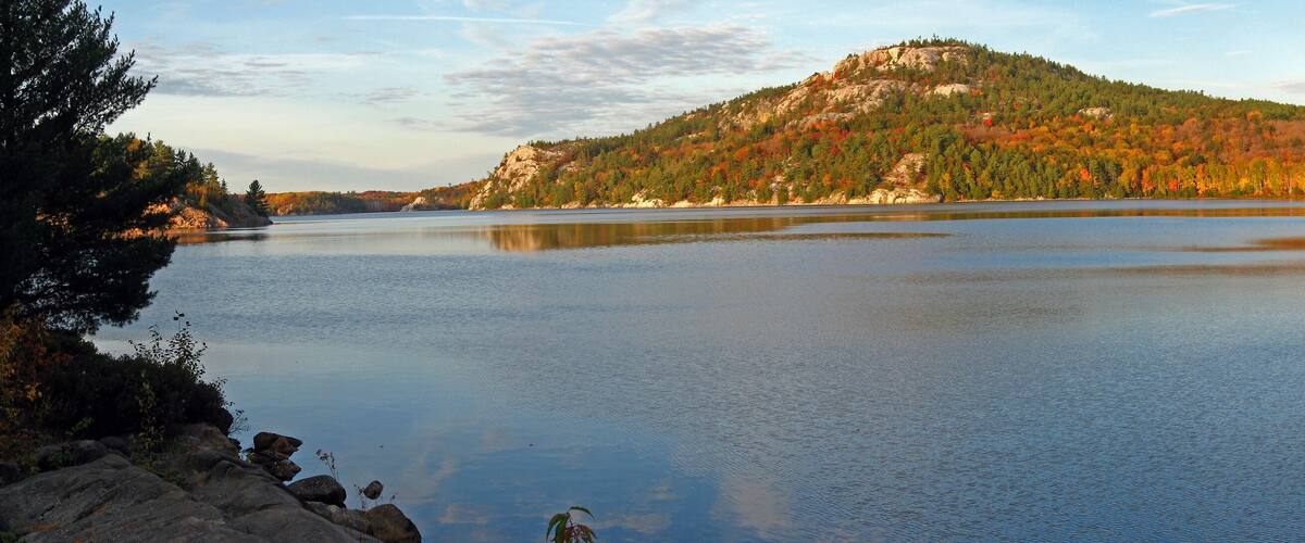 A calm lake surrounded by autumn-colored trees and a rocky hill.