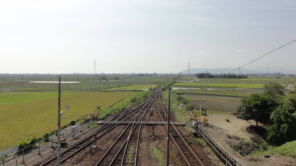 Railway tracks with multiple switches and signals, surrounded by green fields and distant power lines.