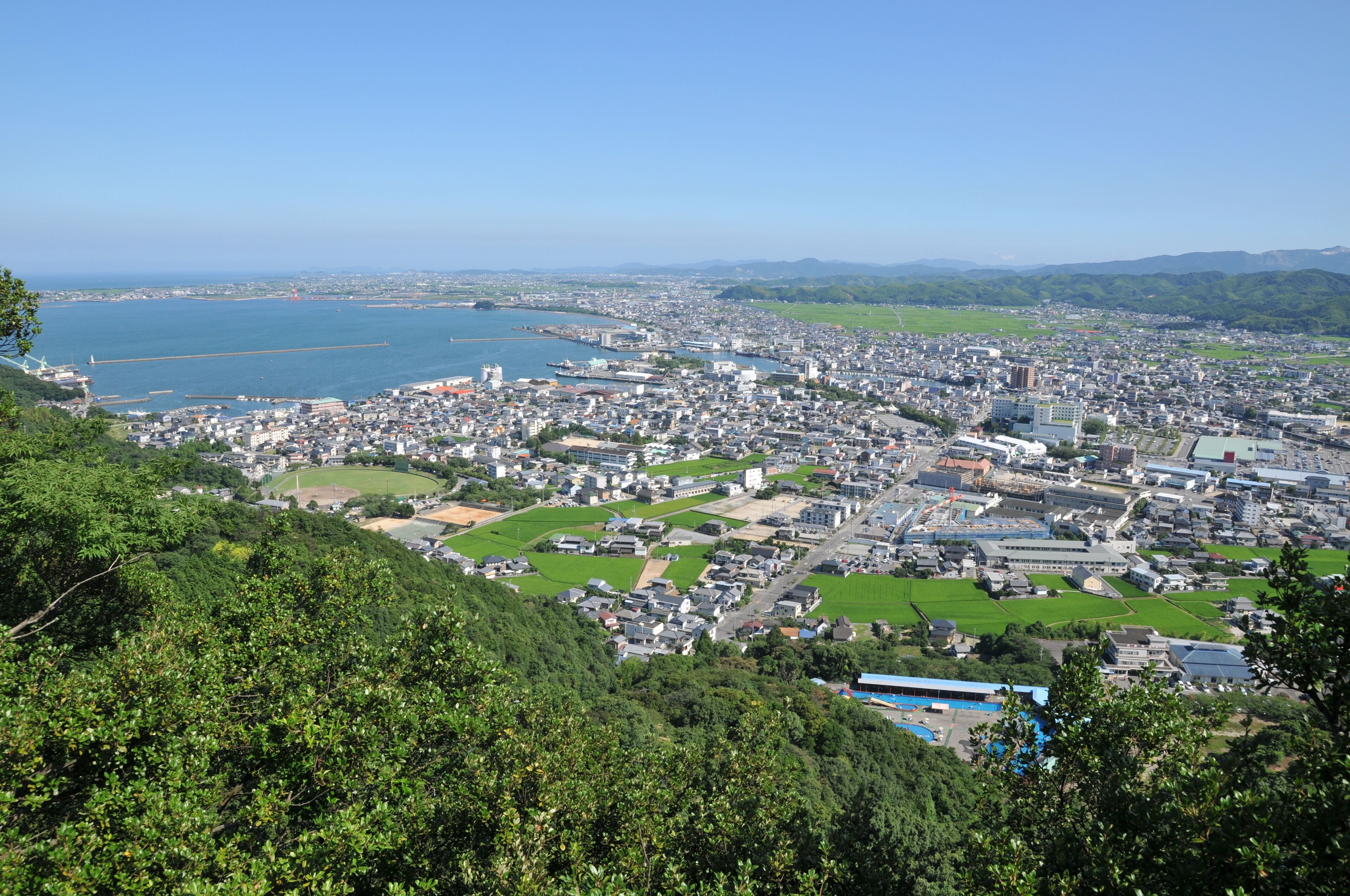 A coastal city with a harbor, green spaces, and a hilly landscape.