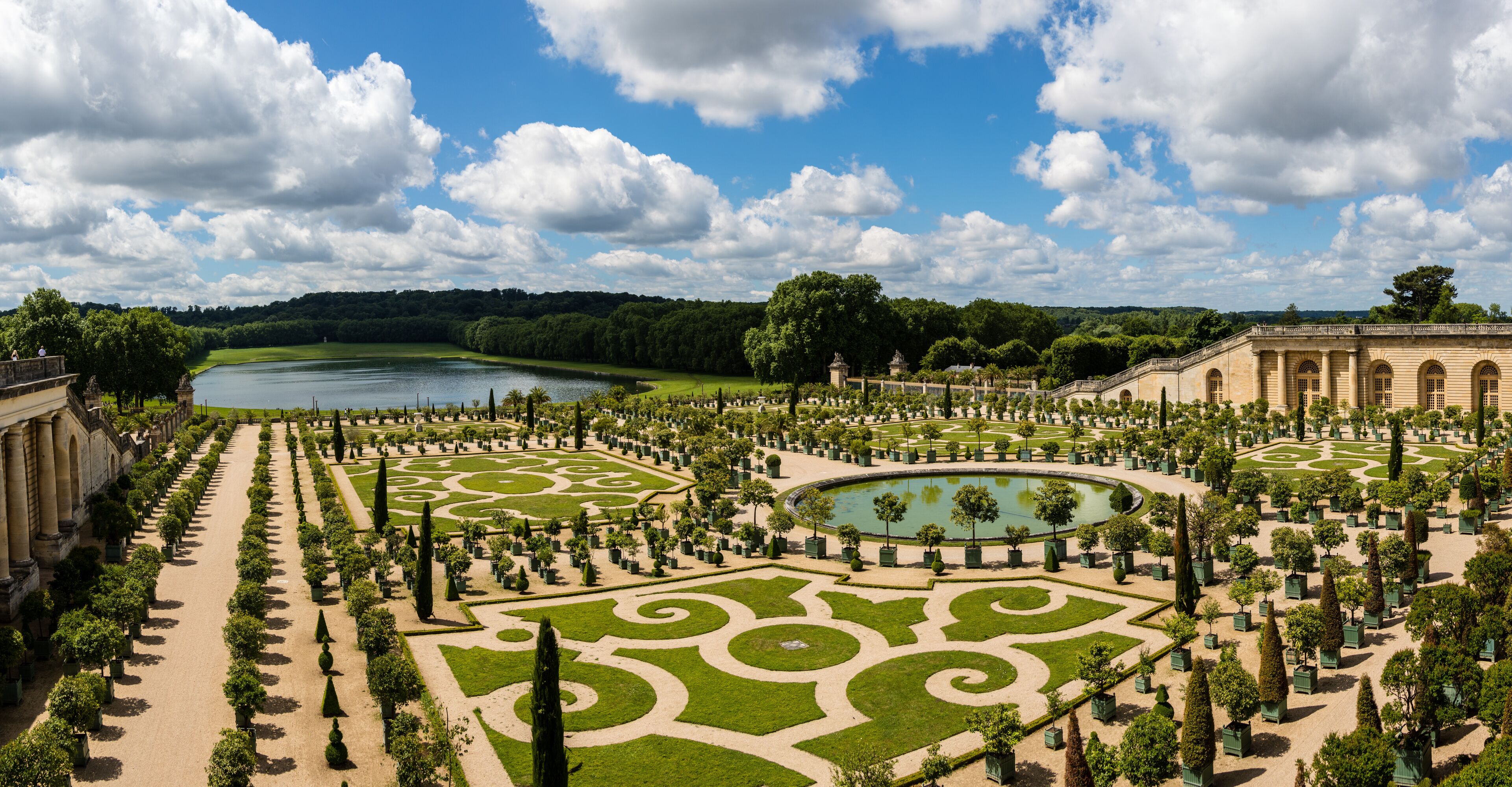 A grand garden with a central pond, manicured lawns, and classical architecture.