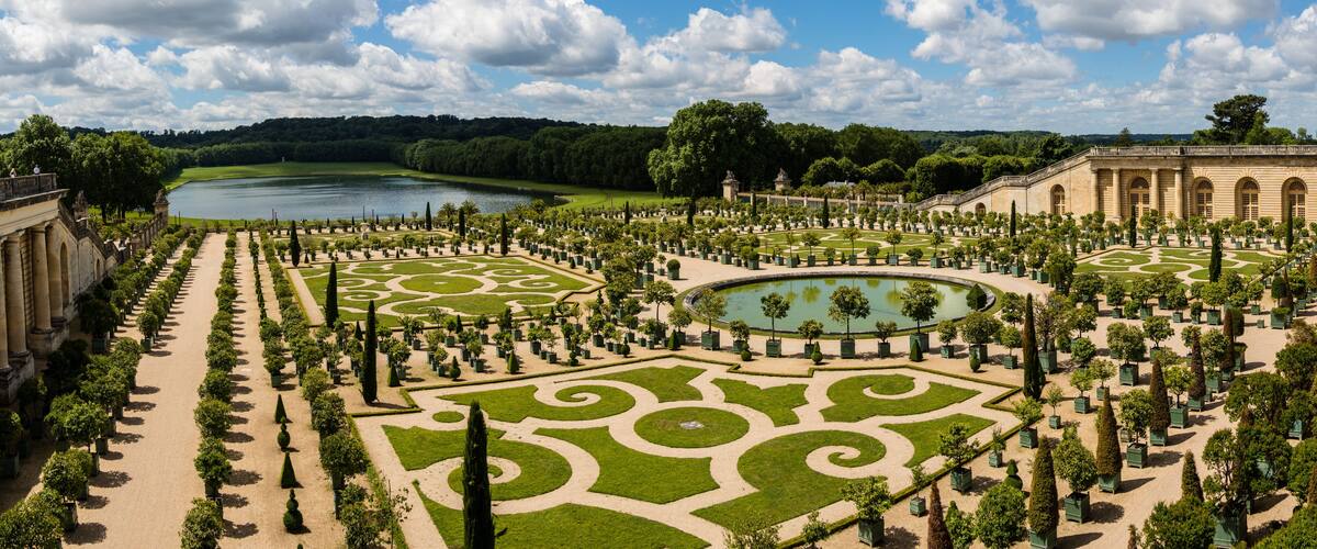 A grand garden with a central pond, manicured lawns, and classical architecture.