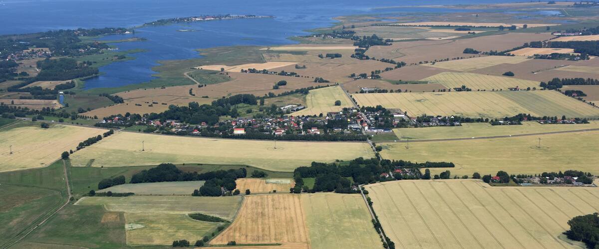An aerial view of a coastal town with fields, a harbor, and a large body of water.