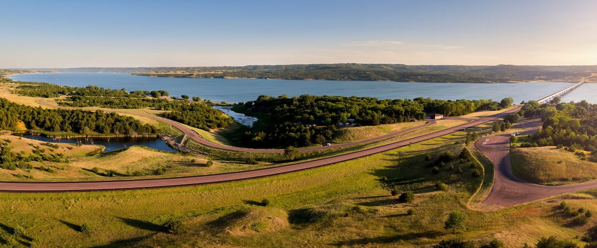 A winding road along a lake with a bridge in the distance.