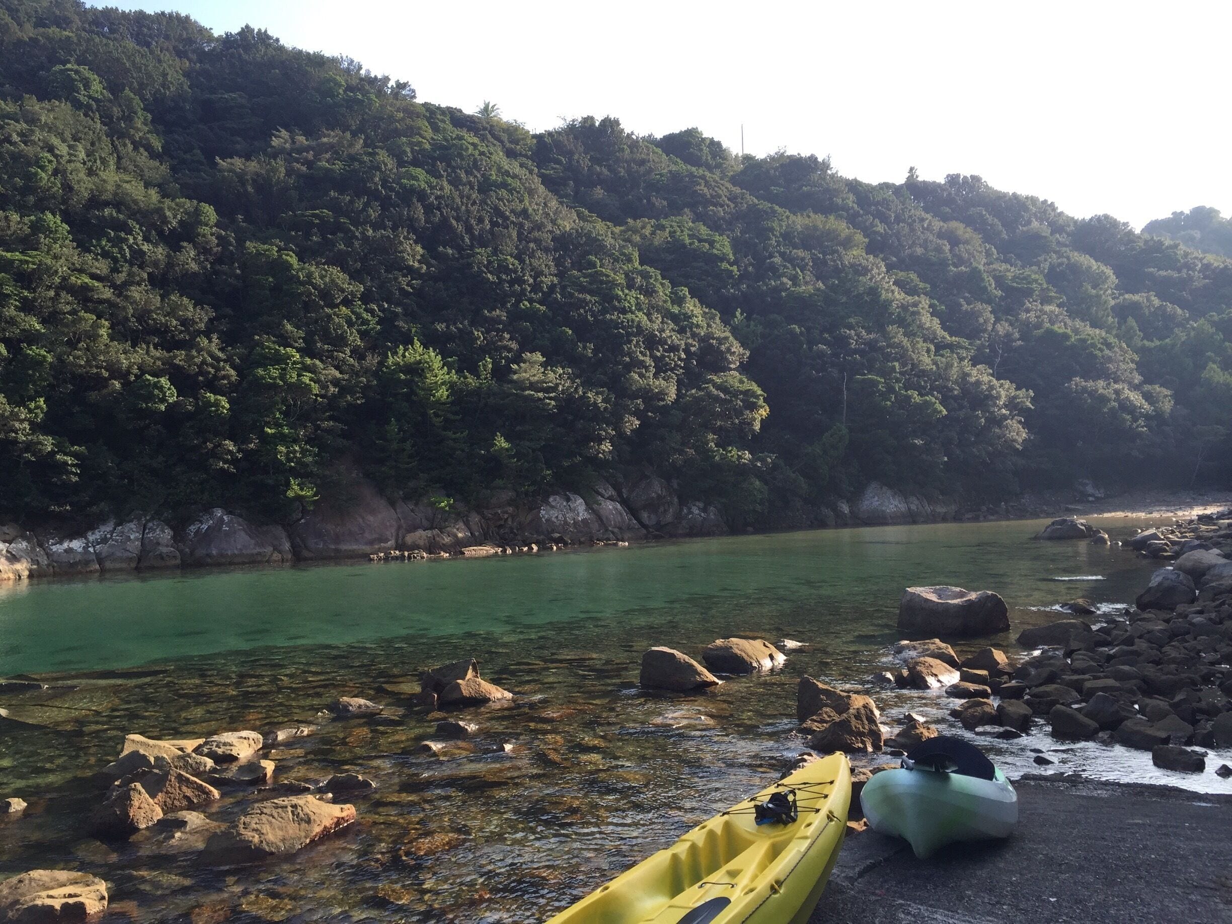 A calm river with clear water, surrounded by rocky shores and dense forested hills.