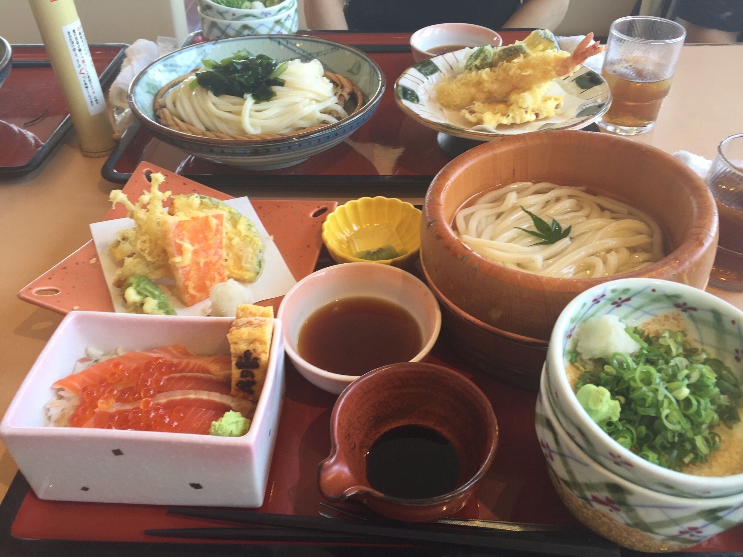 A variety of Japanese dishes on a tray, including bowls of noodles, sashimi, and other seafood.