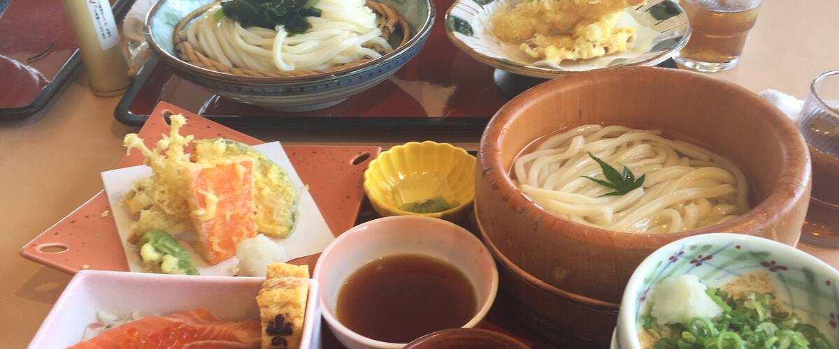 A variety of Japanese dishes on a tray, including bowls of noodles, sashimi, and other seafood.