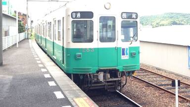 A train at a station with a green and white exterior, platform, and tracks.