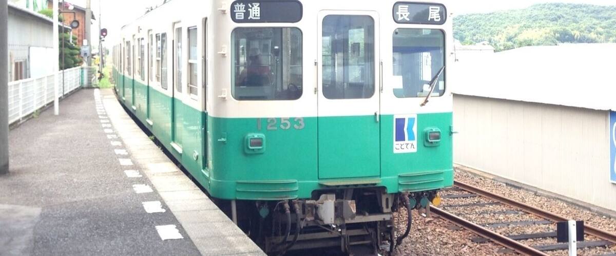 A train at a station with a green and white exterior, platform, and tracks.