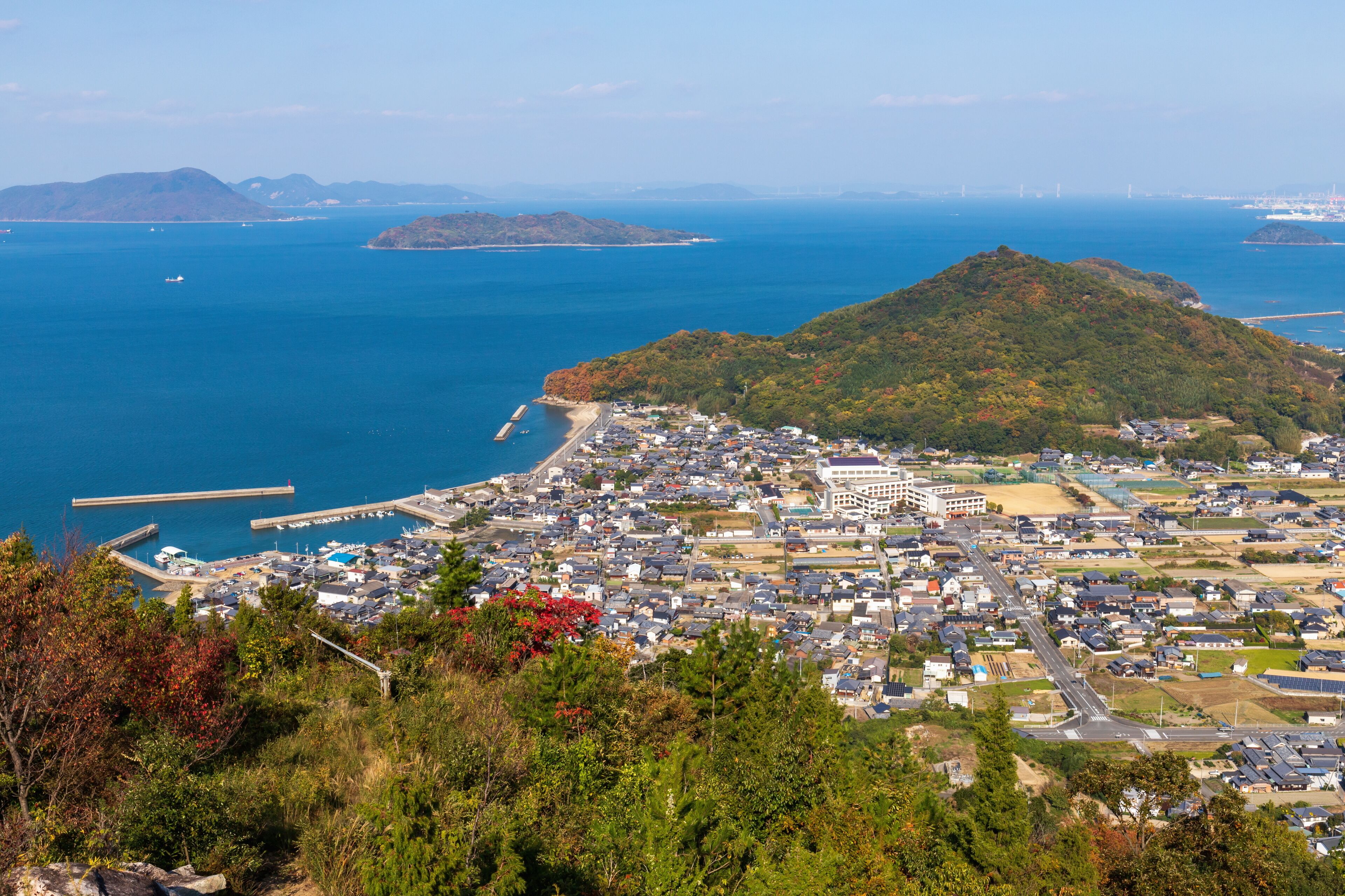 A coastal town with a prominent hill, a pier, and a bridge in the distance.