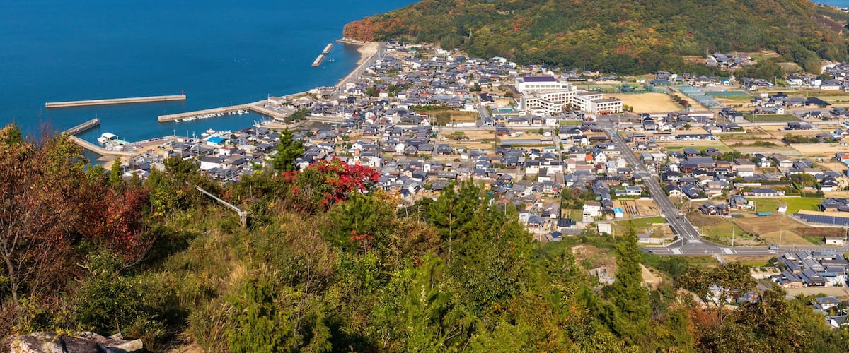 A coastal town with a prominent hill, a pier, and a bridge in the distance.