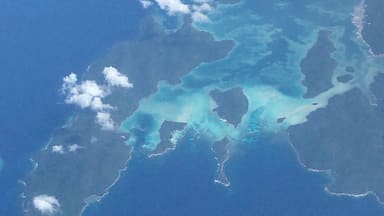 A clear view of a turquoise sea with visible landmasses and cloud formations.