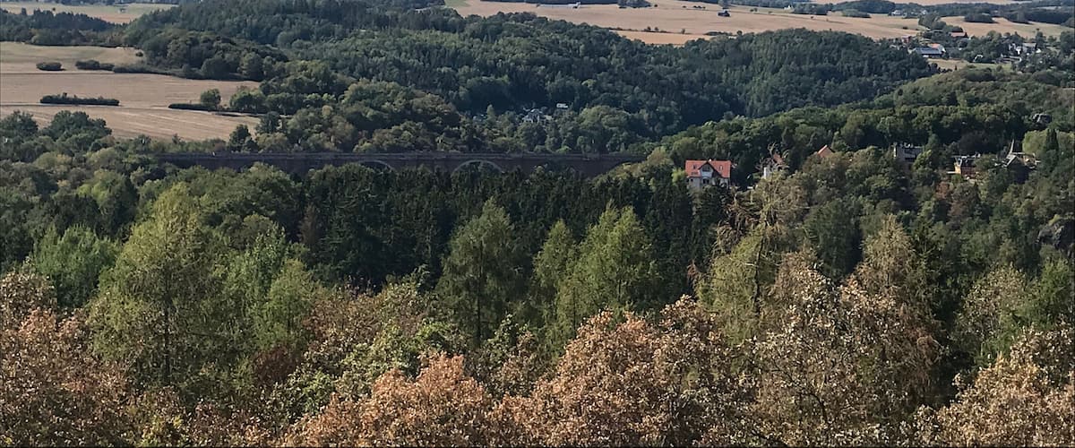 A rural landscape with rolling hills, dense forests, and scattered fields.