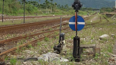 A railway track with a blue and white circular sign, a camera on a tripod, and a mountainous landscape in the background.