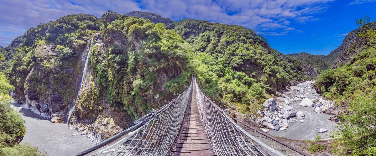 A suspension bridge over a river with steep cliffs and dense greenery.