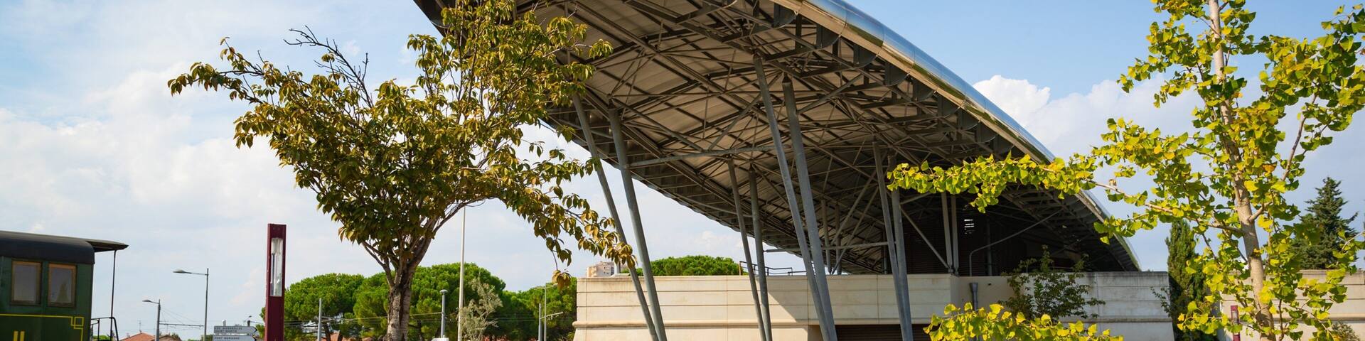 A modern architectural structure with a curved roof, surrounded by a parking area and trees.
